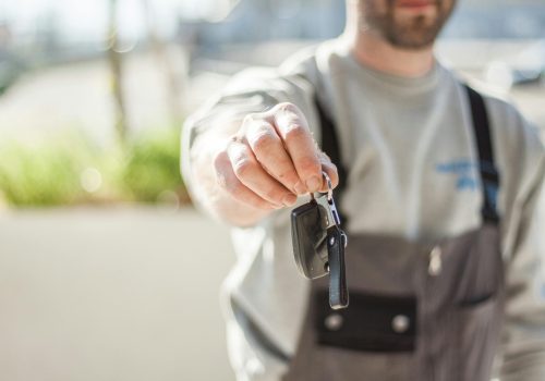 Hand holding a car key outdoors, blurred background, shallow focus.