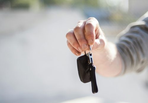 Close-up of a hand handing over car keys, signifying purchase or rental.